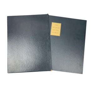 May include: A dark blue book with a matching dark blue slipcase. The book cover features a rectangular gold label with the black text THE WISDOM OF THE FATHERS. The slipcase is plain dark blue and partially covers the book on the left side.