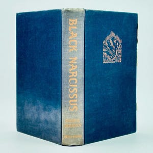 May include: A hardcover book titled "Black Narcissus" by Rumer Godden. The book has a dark blue cover with the title and author's name printed on the spine. A decorative illustration is on the front cover.