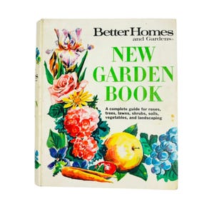 May include: A hardcover book titled Better Homes and Gardens New Garden Book with a white cover featuring colorful illustrations of irises, roses, a yellow apple, blue grapes, and a carrot, along with text about roses, trees, lawns, and shrubs.