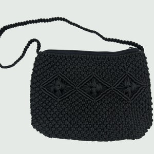 May include: Black macrame shoulder bag with a zipper closure and a knotted strap. The bag features a diamond pattern on the front. The bag is made of a woven material.