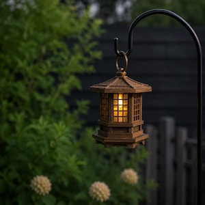 May include: A brown, hexagonal, pagoda-style lantern hanging from a black metal shepherd's hook. The lantern features a slatted wooden frame with a warm, glowing light visible through the central panels, suspended by a circular metal ring.
