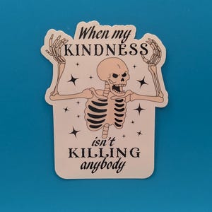 Może przedstawiać: Naklejka z ilustracją szkieletu. Szkielet ma uniesione ramiona i jest otoczony gwiazdami. Tekst na naklejce brzmi: "When my KINDNESS isn't KILLING anybody."