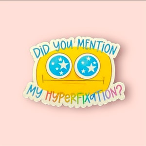 Op de afbeelding: Een gele smiley-sticker met blauwe ogen en witte sterren. De sticker zegt "Did you mention my hyperfixation?"