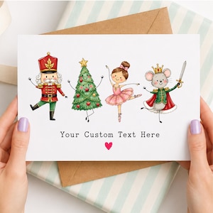 May include: A white greeting card featuring a watercolor illustration of a nutcracker, a decorated Christmas tree, a ballerina in a pink tutu, and a mouse king holding a sword. Below the characters is the text Your Custom Text Here and a small red heart.