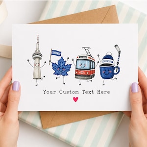 May include: A white greeting card featuring cartoon illustrations of the CN Tower, a blue maple leaf holding a Toronto flag, a red 504 King streetcar, and a blue mug wearing a Toronto beanie with a hockey stick. Text reads Your Custom Text Here.