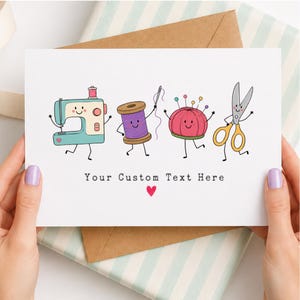 May include: A white greeting card featuring a cartoon illustration of a teal sewing machine, a purple spool of thread with a needle, a pink pincushion, and yellow scissors, all with faces. The text reads Your Custom Text Here with a small red heart.