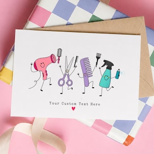 May include: A white greeting card featuring a cartoon illustration of a pink hair dryer, purple scissors, a purple comb, and a teal spray bottle with arms and legs. The text "Your Custom Text Here" is printed below with a small red heart.