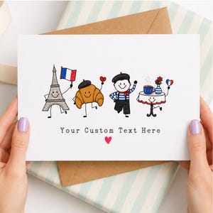 Pode incluir: Um cartão de felicitações branco com uma ilustração de desenho animado da Torre Eiffel com uma bandeira francesa, um croissant com boina, uma pessoa de camisa às riscas com boina e uma mesa com café e flores. O texto diz Your Custom Text Here.