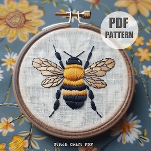Puede incluir: Diseño de abeja bordada en una tela de lino blanco en un aro de bordado de madera. La abeja es negra, amarilla y marrón con puntadas detalladas. El texto "PDF PATTERN" está en un círculo blanco sobre un fondo azul.