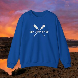 Puede incluir: Sudadera azul real con un gráfico blanco de dos remos cruzados y el texto "SAN JUAN RIVER".