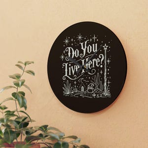 May include: Black round clock with white text that reads "Do You Live Here?" and a white owl illustration. The clock has a white star and wand design.