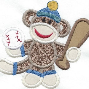 May include: A brown sock monkey wearing a blue hat with a yellow pom-pom, blue jeans, and holding a baseball and a brown bat.