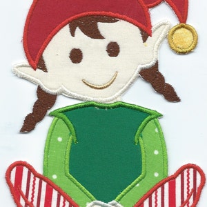 May include: A felt appliqué of a smiling elf wearing a red hat with a gold bell, a green shirt, and red and white striped pants. The elf is sitting with its legs crossed.
