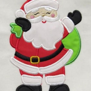 May include: Embroidered applique of a smiling Santa Claus in red and white, holding a green bag. He is wearing a black belt and black boots.