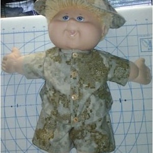 May include: A Cabbage Patch Kid doll wearing a camouflage-patterned shirt, shorts, and hat.