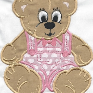 May include: Embroidered brown teddy bear wearing a pink and white polka dot dress with a pink bow.
