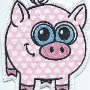 May include: Embroidered patch featuring a cartoon pig with a pink body patterned with white hearts. The pig has large blue eyes, a pink snout, and a curly tail. The patch is outlined in black and white.