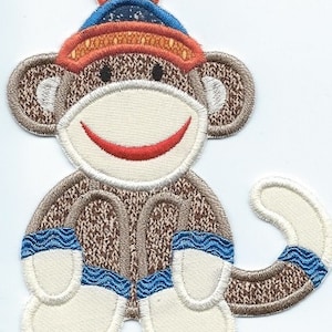 May include: Embroidered patch of a sock monkey wearing a hat and mittens. The monkey is brown with a white face and belly. The hat is orange and blue, and the mittens are blue and white. The monkey has a red smile.