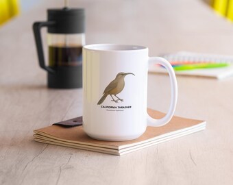 May include: White ceramic mug featuring a detailed illustration of a California Thrasher bird. The bird is depicted in shades of brown and tan, with a long, curved beak. The text "CALIFORNIA THRASHER" is printed below the bird. A French press and notebook are in the background.