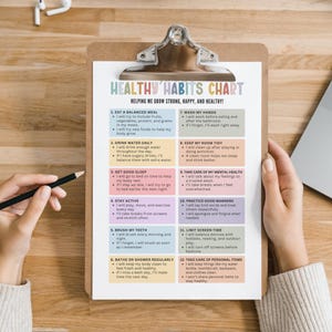 Op de afbeelding: Een klembord met een afgedrukte "Healthy Habits Chart" in een kleurrijk ontwerp. De tabel bevat 12 gewoonten voor een gezonde levensstijl, waaronder het eten van evenwichtige maaltijden, het drinken van water en voldoende slaap. Een potlood wordt in de buurt van de tabel gehouden.