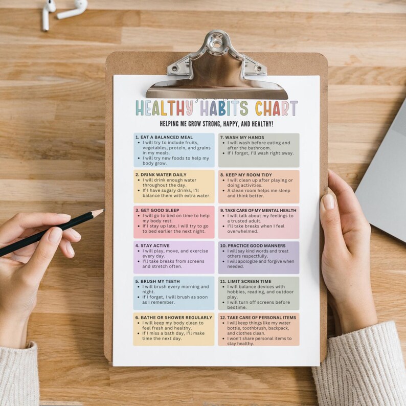 Op de afbeelding: Een klembord met een afgedrukte "Healthy Habits Chart" in een kleurrijk ontwerp. De tabel bevat 12 gewoonten voor een gezonde levensstijl, waaronder het eten van evenwichtige maaltijden, het drinken van water en voldoende slaap. Een potlood wordt in de buurt van de tabel gehouden.