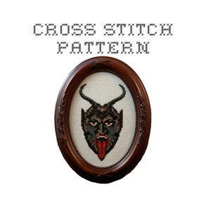 May include: Cross stitch pattern of a devil's face with red horns, black eyes, and a red tongue. The pattern is framed in a dark brown oval frame.