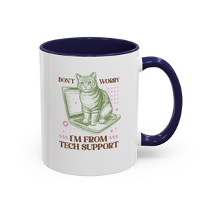 May include: White ceramic mug with a blue rim and handle. The mug features a green illustration of a cat sitting on a laptop with the text "Don't Worry I'm From Tech Support" in brown and pink.