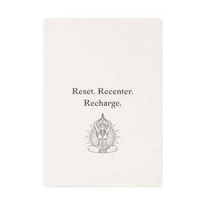Op de afbeelding: Een witte theedoek met de tekst "Reset. Recenter. Recharge." en een zwart-witte illustratie van een persoon in een yogahouding.