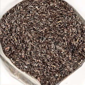 Può includere: Primo piano di un sacchetto di plastica trasparente pieno di materiale vegetale secco e tritato. Il materiale è principalmente marrone scuro con pezzi marroni chiari e beige. La consistenza appare ruvida e fibrosa.