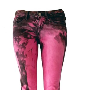 Könnte beinhalten: Rosa und schwarze Tie-Dye-Jeans. Die Jeans haben einen ausgewaschenen Look mit einem dunklen, schwarzen Tie-Dye-Muster auf rosa Hintergrund.