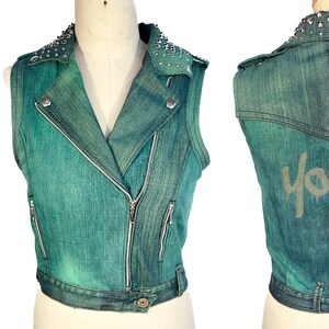 May include: A teal blue denim vest with silver studs on the collar and a zipper closure. The vest has a "Youth" graphic on the back.