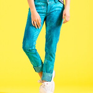 May include: A person wearing blue jeans with a tie-dye pattern and white sneakers on a yellow background.