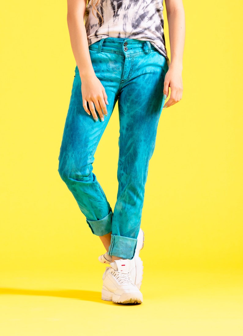 May include: A person wearing blue jeans with a tie-dye pattern and white sneakers on a yellow background.