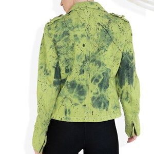 May include: A green denim jacket with black splatter paint. The jacket has a zipper closure and a collar.