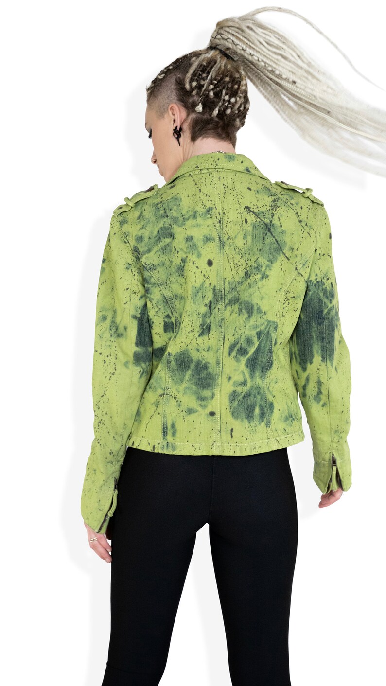 May include: A green denim jacket with black splatter paint. The jacket has a zipper closure and a collar.