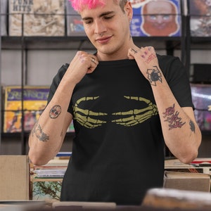 May include: A person with pink hair is wearing a black t-shirt with a green skeleton hand graphic. The t-shirt has the text "Don't Worry Be Happy" on the left sleeve.