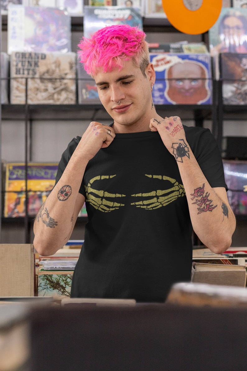 May include: A person with pink hair is wearing a black t-shirt with a green skeleton hand graphic. The t-shirt has the text "Don't Worry Be Happy" on the left sleeve.