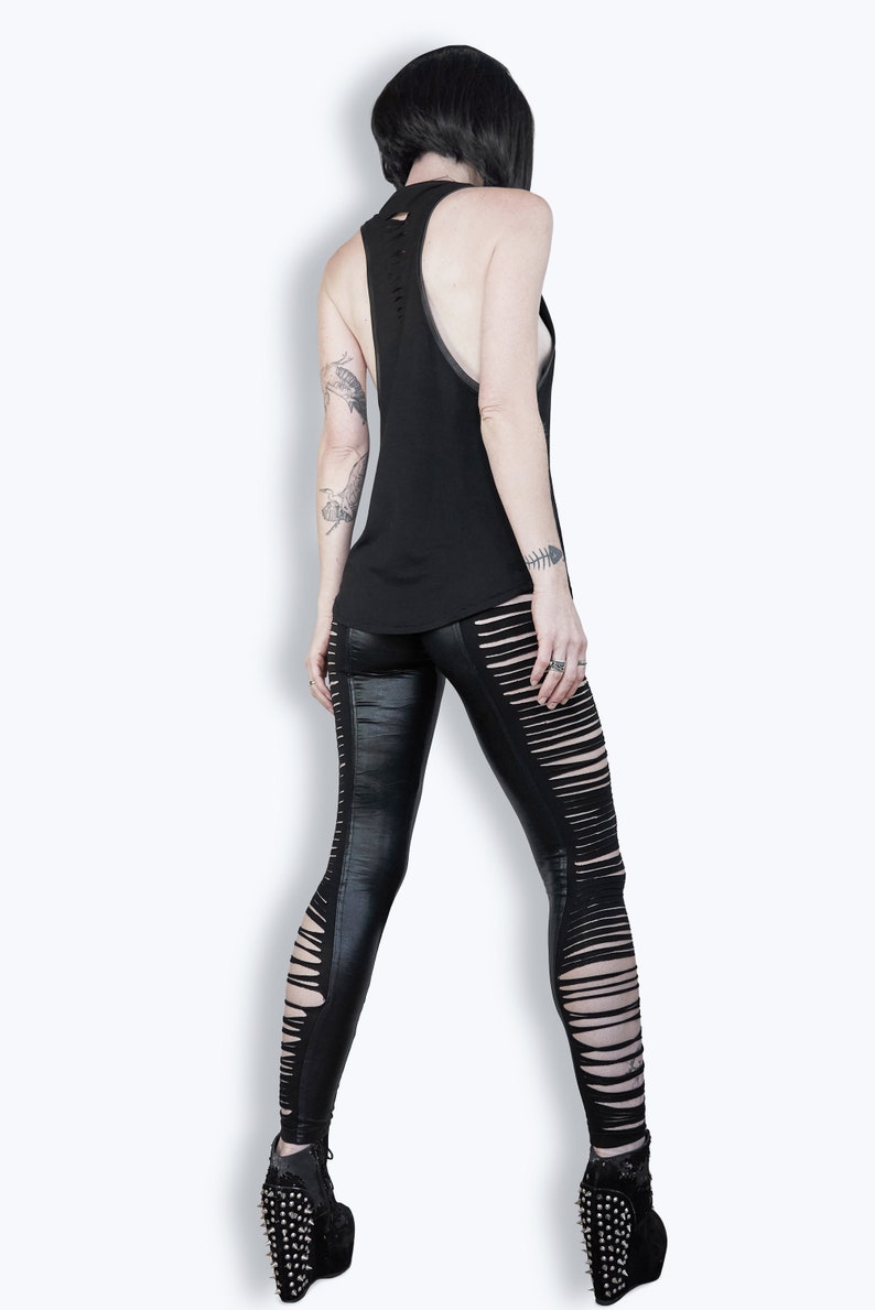 May include: A black sleeveless tank top with a distressed back and a pair of black leggings with cutouts on the sides. The leggings are worn with black platform shoes.