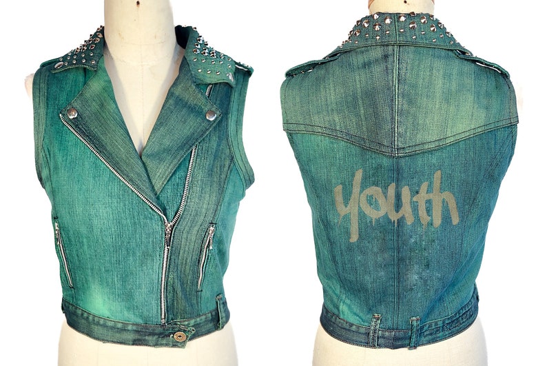 May include: A teal blue denim vest with silver studs on the collar and a zipper closure. The vest has a "Youth" graphic on the back.
