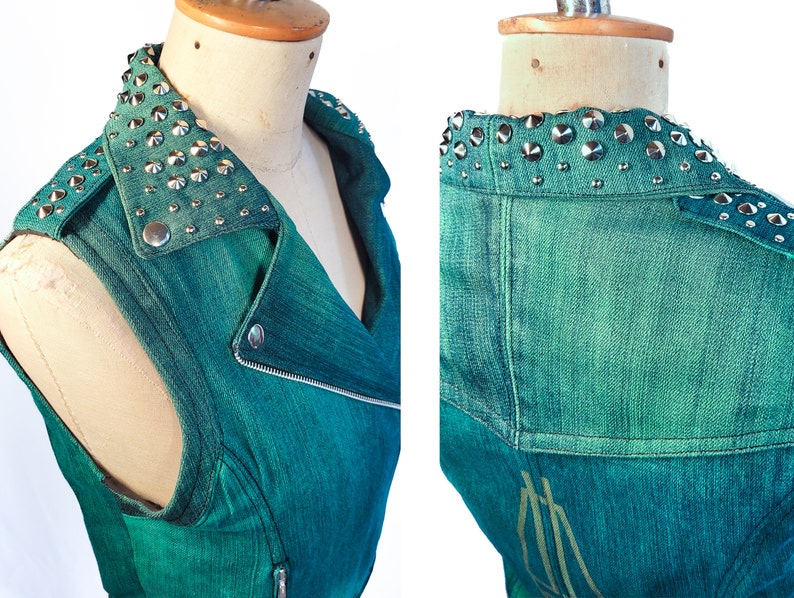 May include: Teal denim sleeveless vest with a studded collar. The vest has a zipper closure and a biker-style design.