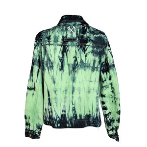 May include: A green and black tie-dye denim jacket with a button closure and long sleeves. The jacket has a white cross stitched on the back.