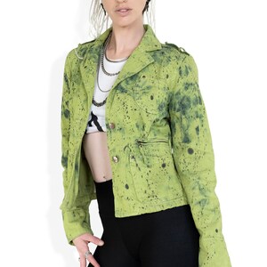 May include: A green splatter-painted denim jacket with a zippered pocket and button closure.
