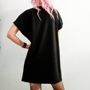 May include: A black short-sleeved dress with a loose fit. The dress is worn over black fishnet tights with holes in the fabric.