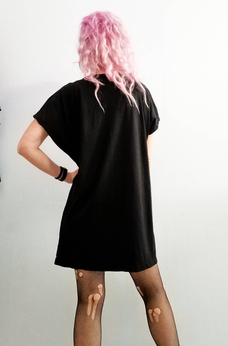May include: A black short-sleeved dress with a loose fit. The dress is worn over black fishnet tights with holes in the fabric.