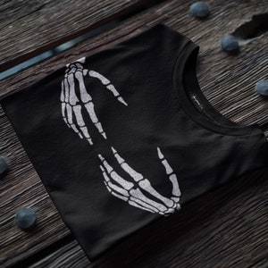 May include: Black t-shirt with a white skeleton hand design. The hands are facing each other and appear to be holding something.