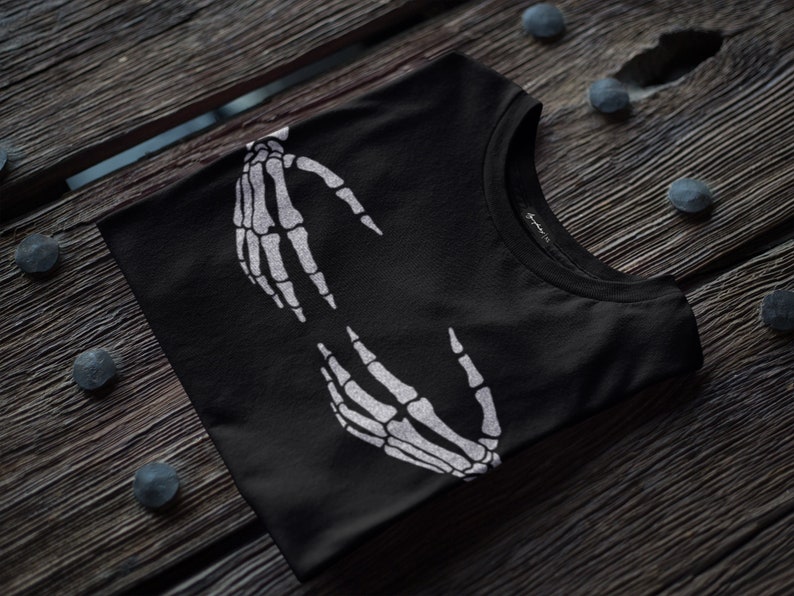 May include: Black t-shirt with a white skeleton hand design. The hands are facing each other and appear to be holding something.