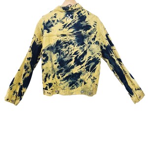 Pu&ograve; includere: Giacca di jeans gialla con motivo tie-dye blu navy. La giacca ha un colletto classico, bottoni e maniche lunghe. Un disegno ricamato bianco &egrave; sulla parte superiore della schiena. La giacca &egrave; esposta su una gruccia di legno.