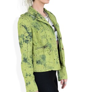 May include: A green denim jacket with a splatter paint design. The jacket has a zipper closure and two pockets.