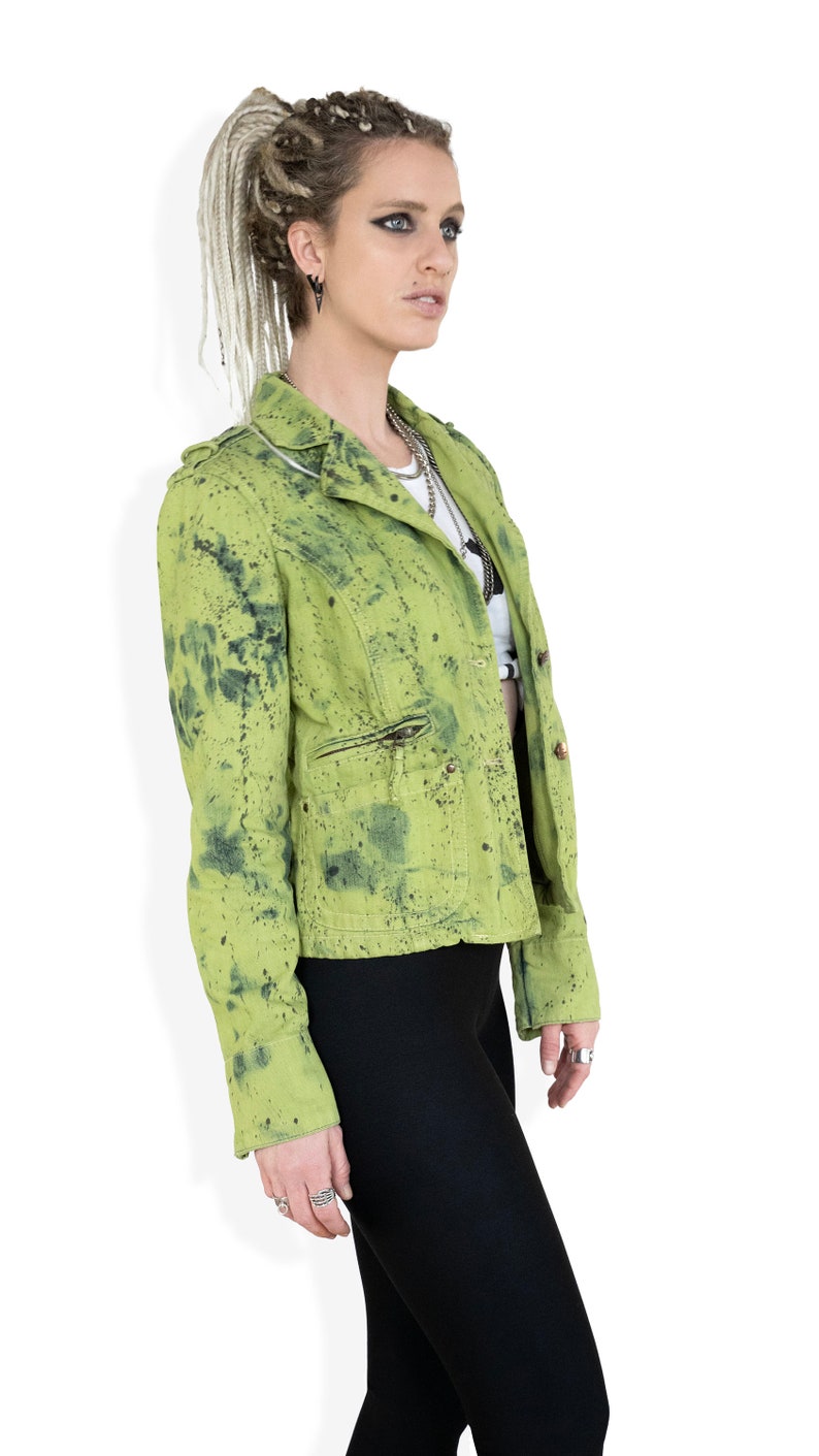 May include: A green denim jacket with a splatter paint design. The jacket has a zipper closure and two pockets.