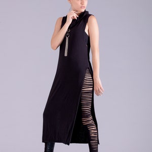 May include: A woman wearing a black maxi dress with a side slit and black leggings with cutouts. She is wearing black heeled boots and has her hair pulled back in a bun.